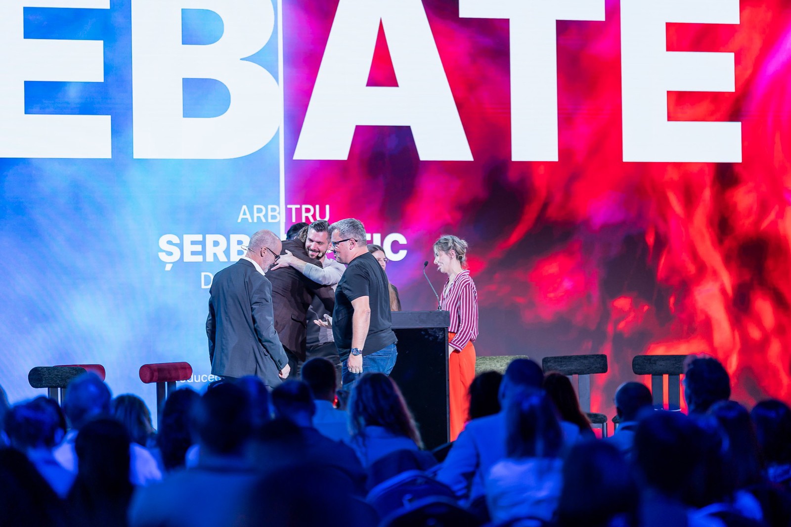 Participanții la dezbatere se îmbrățișează și se felicită pe scenă, la final